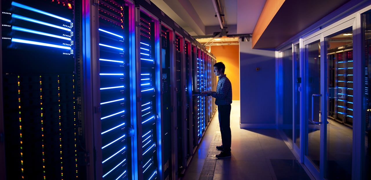 A lone figure working in a server room, lit only by the servers