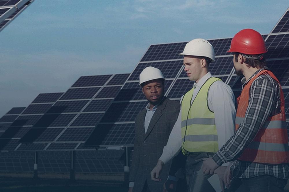 Men standing in front of solar panels wearing hard hats.